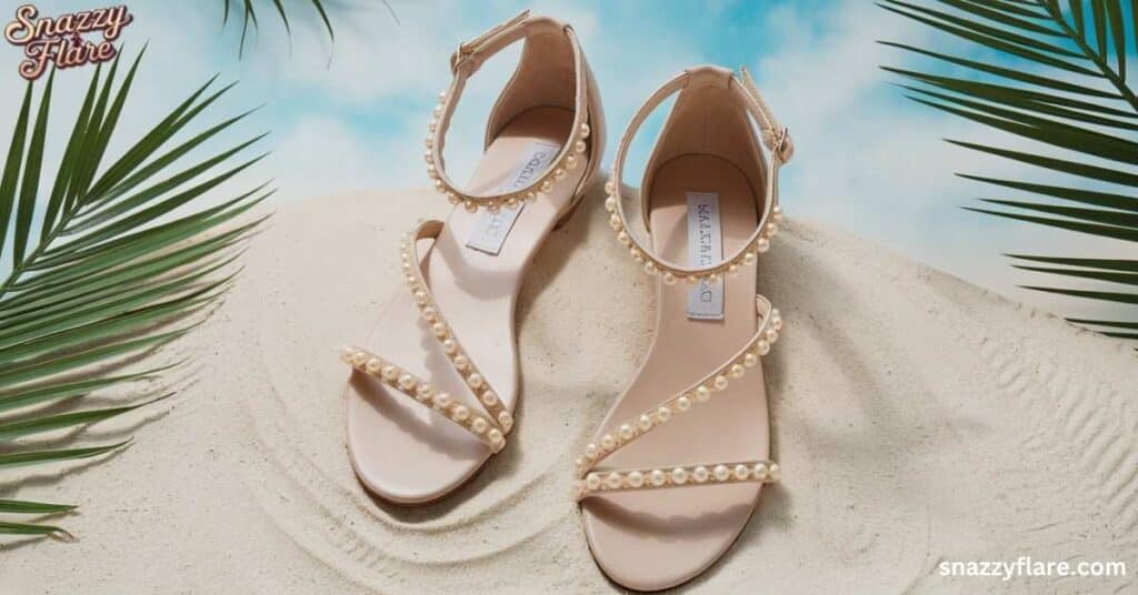 Beige sandals with pearl embellishments on straps, displayed on sand."