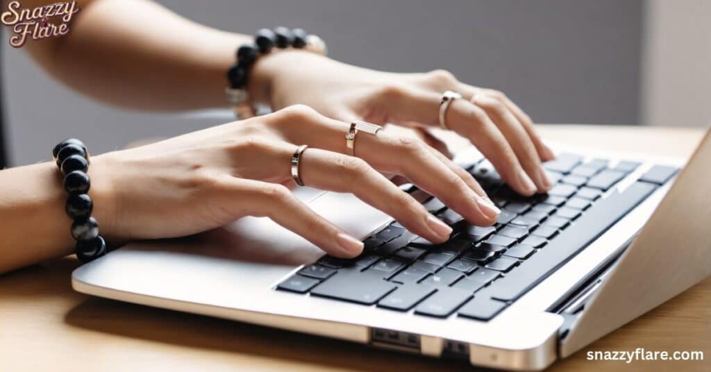 Hands adorned with rings and bracelets typing on a laptop keyboard