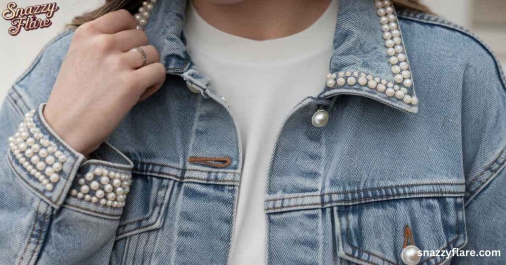 Close-up of a denim jacket with pearl embellishments on collar and cuffs, worn over a white shirt