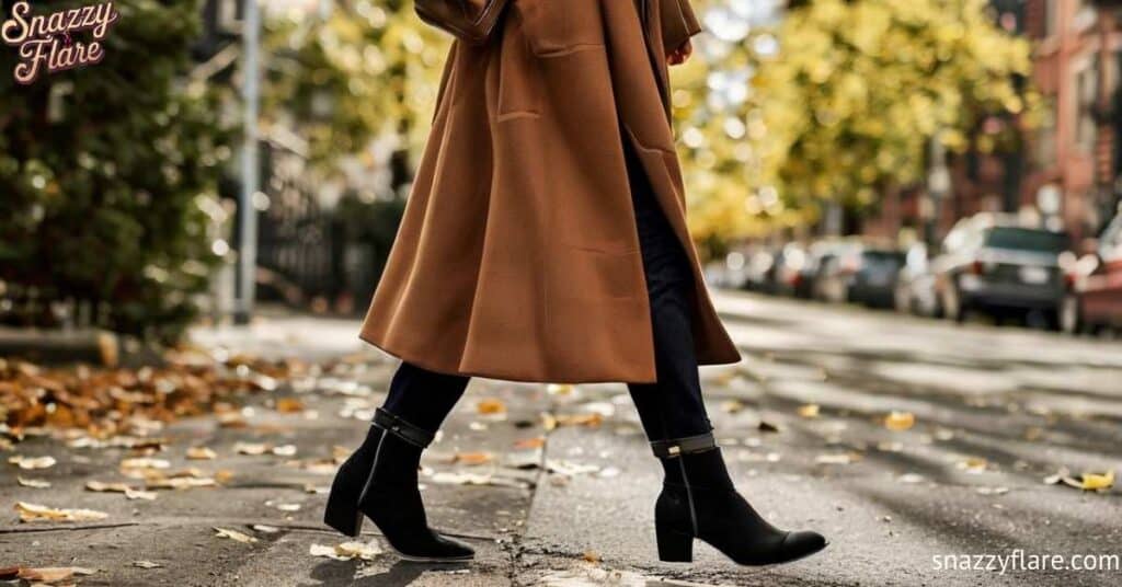 Women walking on a leaf-strewn street wearing a long brown coat and black ankle boots