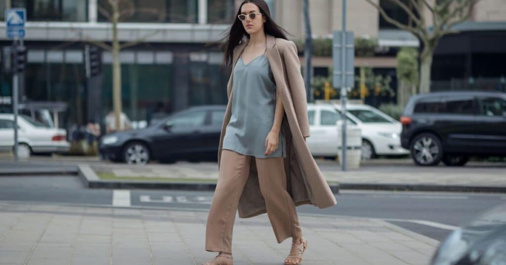 A person wearing a slip dress, straight-leg trousers, and strappy sandals, with a minimalist and chic aesthetic