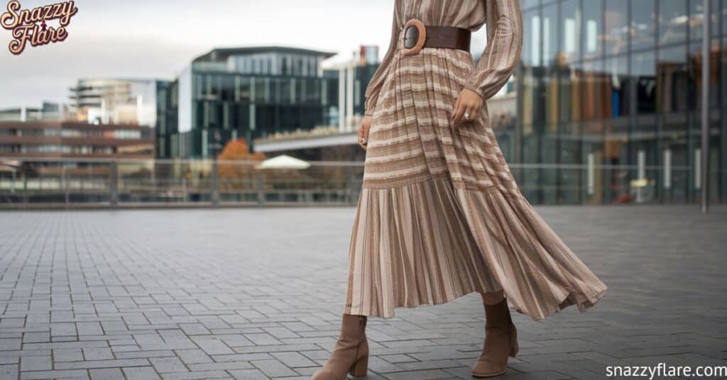 A woman in a long, patterned dress and boots is walking in an urban area with modern glass buildings in the background.